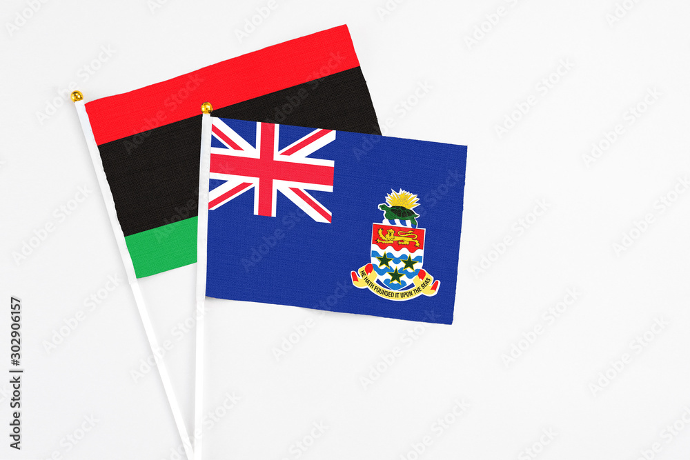 Fototapeta premium Cayman Islands and Libya stick flags on white background. High quality fabric, miniature national flag. Peaceful global concept.White floor for copy space.