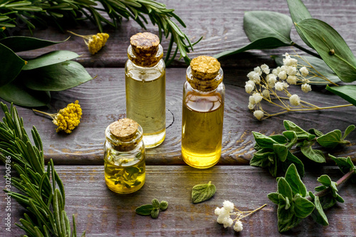 Aromatherapy. Essential oils in small bottles near fresh herbs on dark wooden background