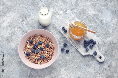 Healthy food background with homemade oatmeal granola or muesli, bottle of milk, honey and fresh berries for healthy morning breakfast, top view, copy space. Selective focus.          
