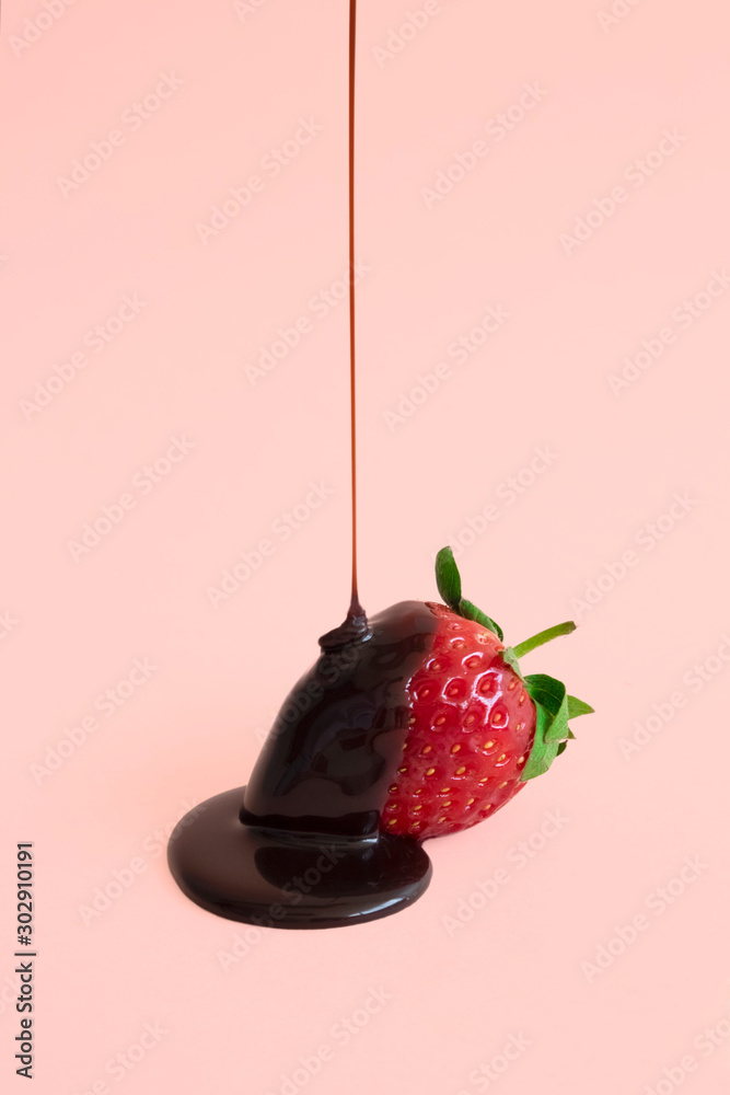 Fototapeta Minimalna kropla ciemnej czekolady przelewająca się do czerwonych truskawek na pastelowo różowym tle