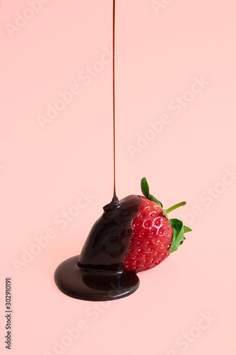 Minimal dark chocolate pouring drop to red strawberries on pastel pink background