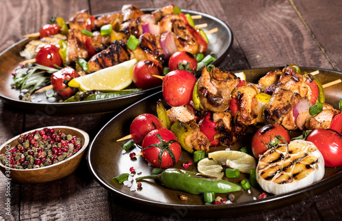 Grilled chicken skewers with spices and vegetables in a pans on wooden background