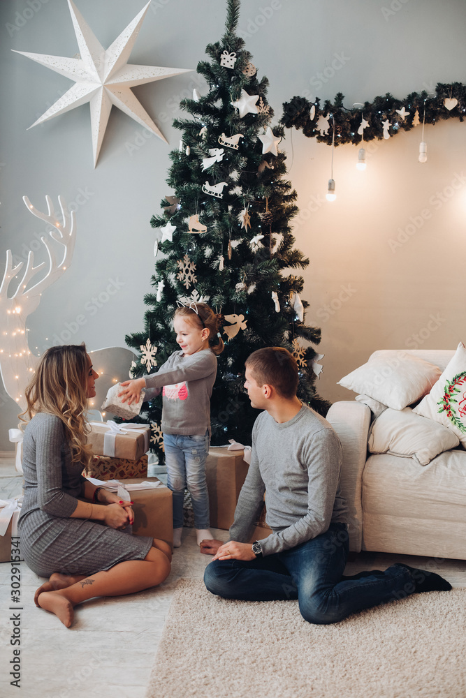 Stock photo ful length portrait of happy young family with cute little daughter sitting on cozy couch with cushions and smiling at camera. Little girl holding decorative star in hands. They are Stock photo ful length portrait of happy young family with cute little daughter sitting on cozy couch with cushions and smiling at camera. Little girl holding decorative star in hands. They are