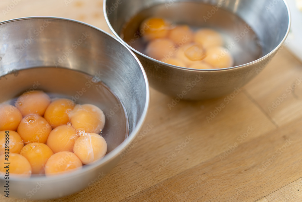 Two stainless steel bowls filled with many cracked eggs with whole yolks, in the wooden table. Close up Two stainless steel bowls filled with many cracked eggs with whole yolks, in the wooden table. Close up