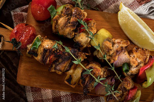 Grilled chicken skewers with spices and vegetables on cutting board and wooden background