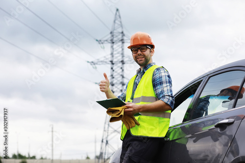 A man in a helmet and uniform, an electrician in the field. Professional electrician engineer inspects power lines during work. © alexkich