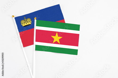 Suriname and Liechtenstein stick flags on white background. High quality fabric, miniature national flag. Peaceful global concept.White floor for copy space.