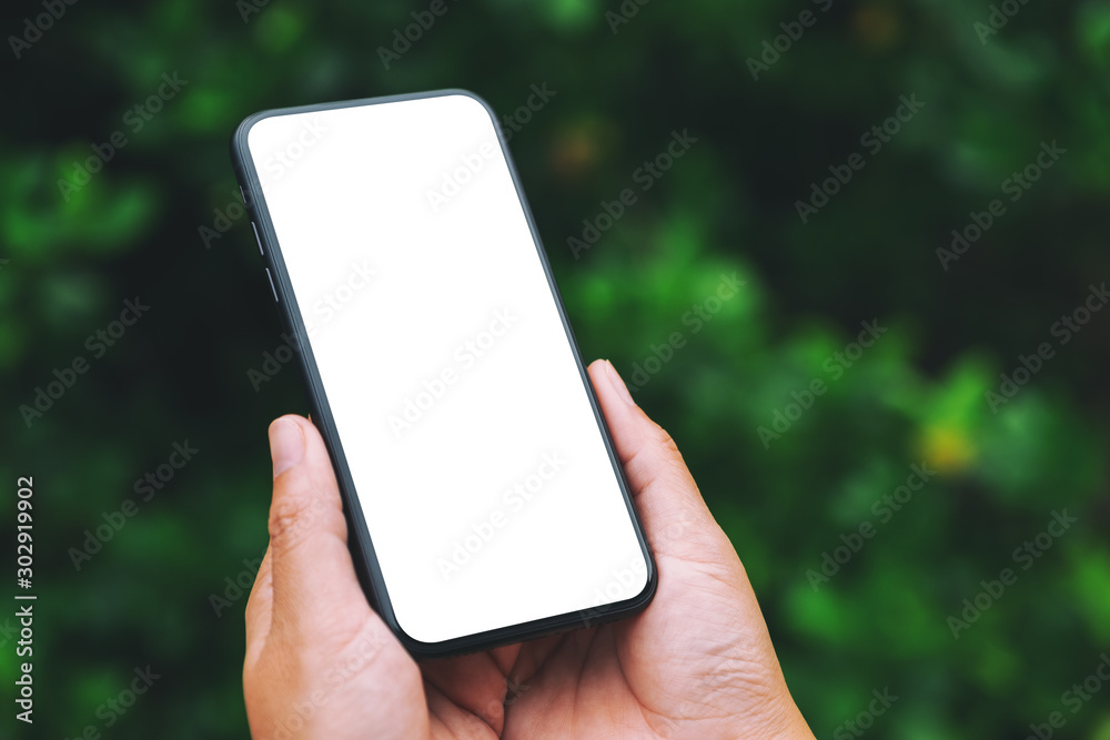 Mockup image of hands holding black mobile phone with blank desktop screen with green nature background