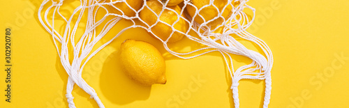 top view of fresh ripe whole lemons in eco string bag on yellow background, p...