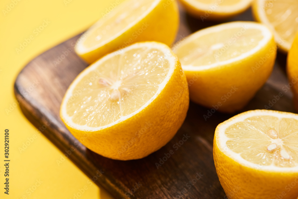 close up view of ripe cut lemons on wooden cutting board on yellow background close up view of ripe cut lemons on wooden cutting board on yellow background
