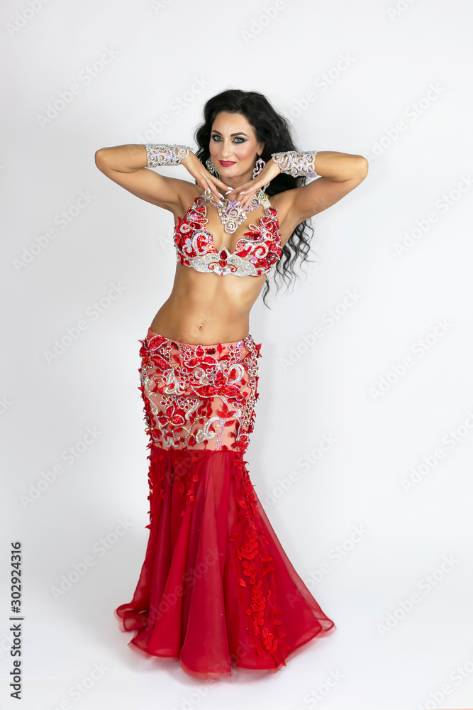 Brunette in a beautiful long red dress perform belly dance on a white background Girl in a red dress for oriental dancing.