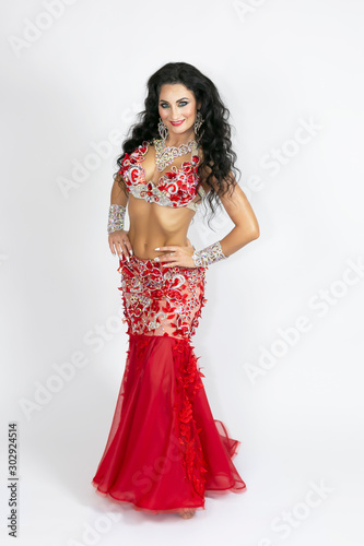 Girl in a red dress for oriental dancing. Brunette in a beautiful long red dress to perform belly dance on a white background