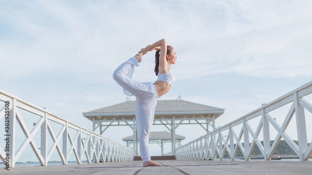 Young women practice yoga on the white bridge by the sea, the concept of enjoying privacy and the concentration of sunlight.