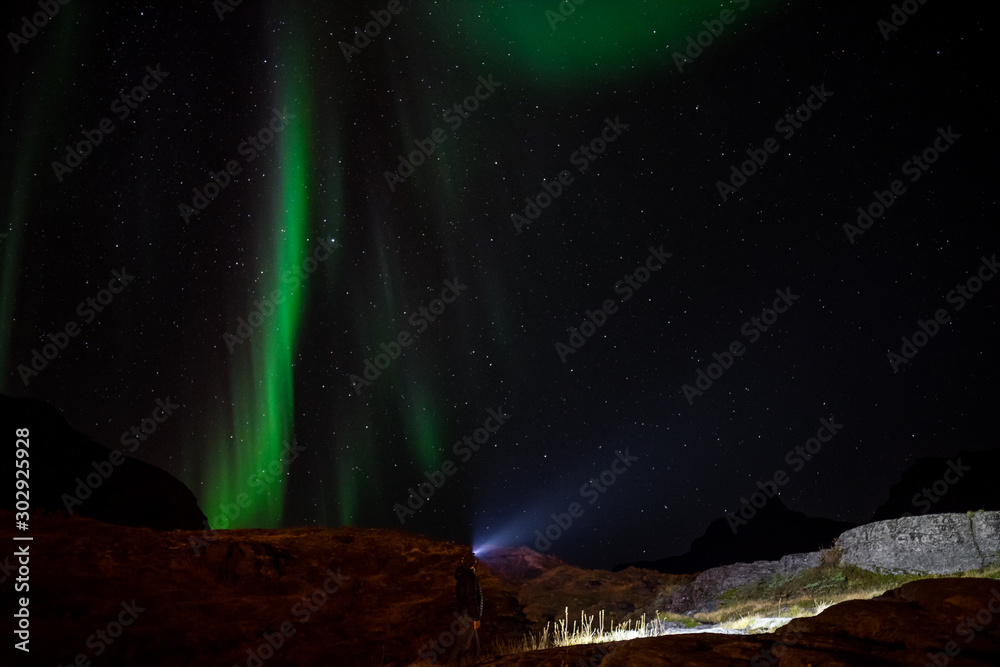 Man with flashlight watching northern lights on sky