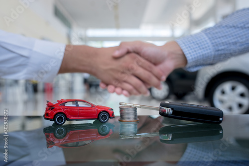 Agreements to buy new cars  new car loans or signing contracts with car keys and money in the foreground Blurred background for two business people standing hand in hand