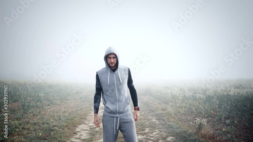 Sporty fit young man walking into the frame in the middle with foggy background, motivational (ID: 302930961)