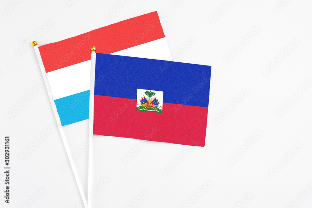 Haiti and Luxembourg stick flags on white background. High quality fabric, miniature national flag. Peaceful global concept.White floor for copy space.