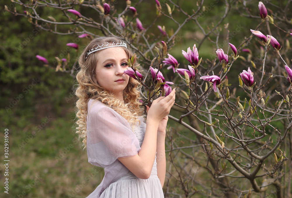 Fototapeta premium young beautiful girl in a light lilac dress in the garden where magnolias bloom