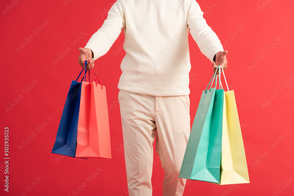 cropped view of man holding colourful shopping bags isolated on red