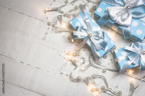Blue gift boxes and lights with pearls on white wooden background