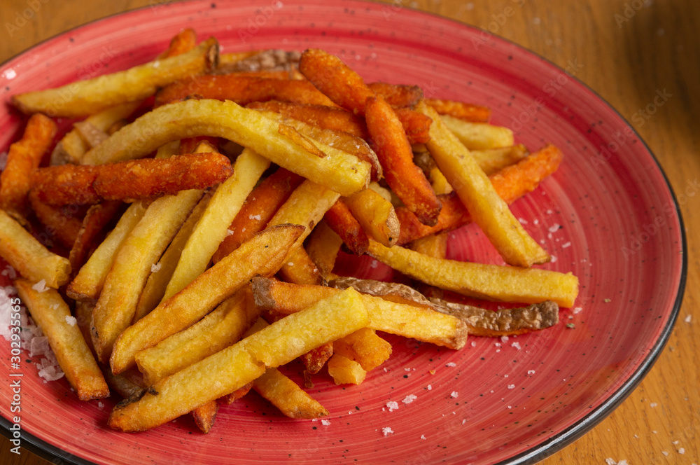 Plate of fried potatoes with sweet potato and coarse salt served on red ceramic plate on wooden background Plate of fried potatoes with sweet potato and coarse salt served on red ceramic plate on wooden background