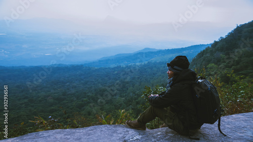 Asian man travel nature. Travel relax. Sit and watch nature landscapes on the cliff. Vacation on the mountains. Admire the atmosphere landscape on travel Thailand.