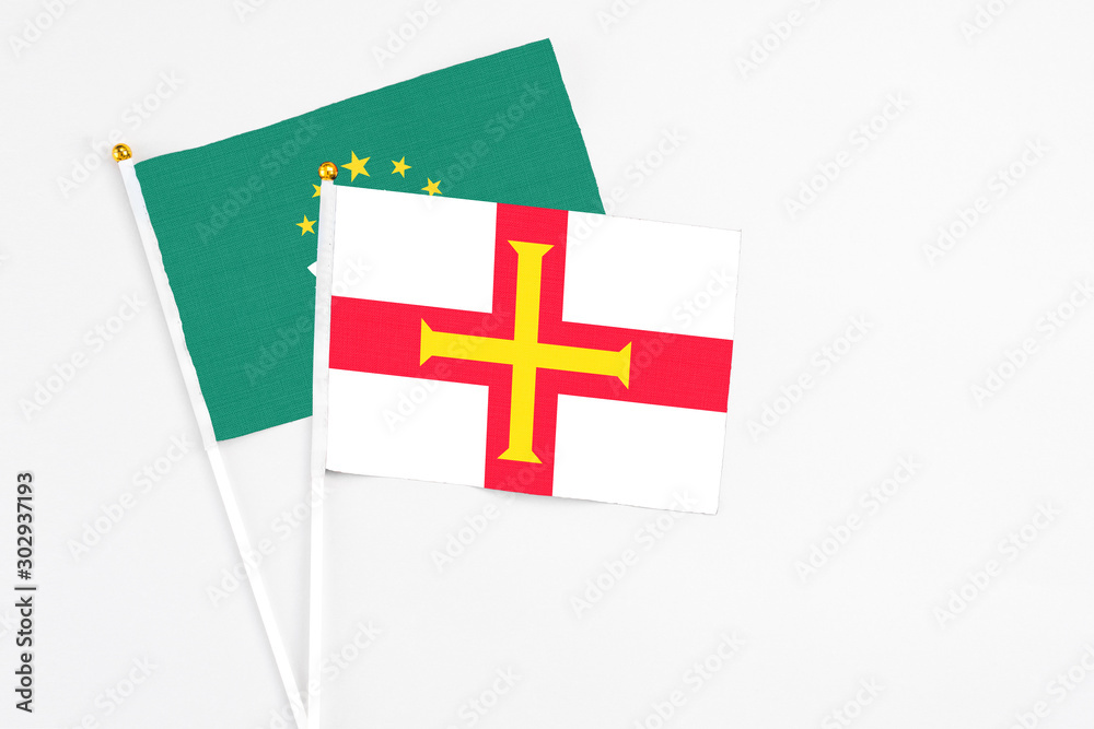 Guernsey and Macao stick flags on white background. High quality fabric, miniature national flag. Peaceful global concept.White floor for copy space.