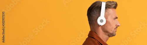 panoramic shot of handsome man in wireless headphones listening music isolated on orange