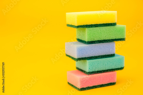 Multicolored sponges for cleaning folded pyramid on a yellow background. Space for text