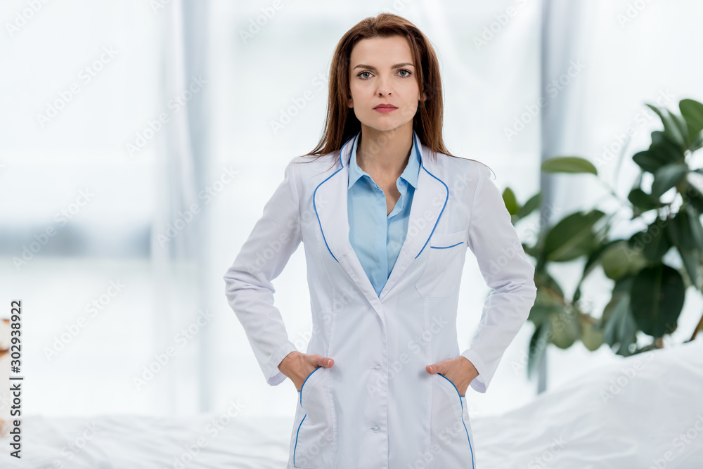 attractive doctor in white coat with hands in pockets looking at camera in hospital attractive doctor in white coat with hands in pockets looking at camera in hospital