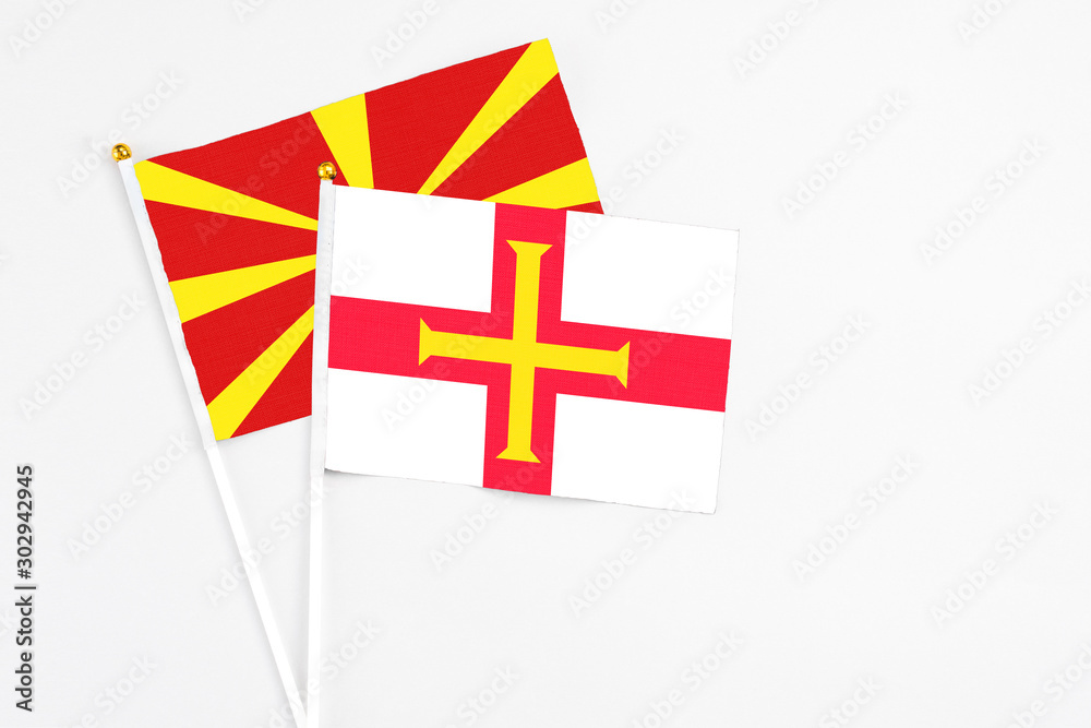 Guernsey and Macedonia stick flags on white background. High quality fabric, miniature national flag. Peaceful global concept.White floor for copy space.