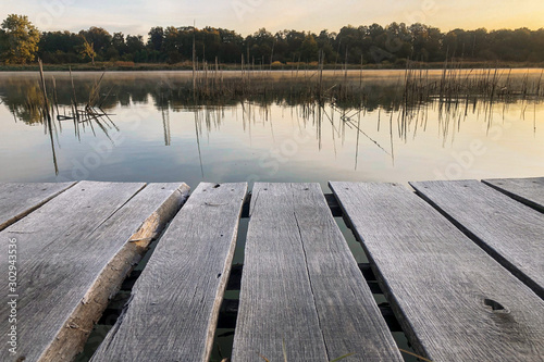 Wood masonry on the lake. Morning with light fog. Rotten pier on the shore of a calm reservoir. Shore reflection. © yatsiuk