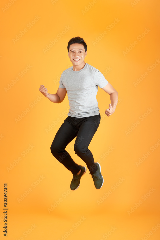 Energetic happy young Asian man in casual clothes jumping, studio shot isolated in orange background Energetic happy young Asian man in casual clothes jumping, studio shot isolated in orange background