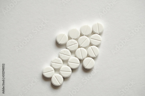 Abstract signs and symbols of growth, business development, profit. White pharmaceutical drug pills stacked on a flat white surface in the shape of an arrow pointing up and forward.