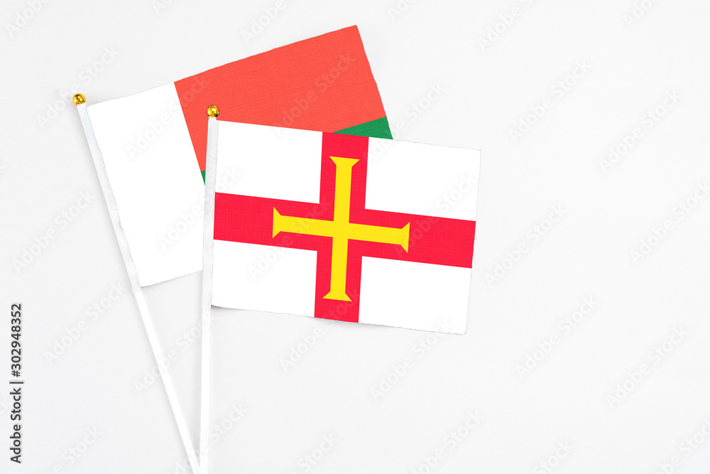 Guernsey and Madagascar stick flags on white background. High quality fabric, miniature national flag. Peaceful global concept.White floor for copy space.