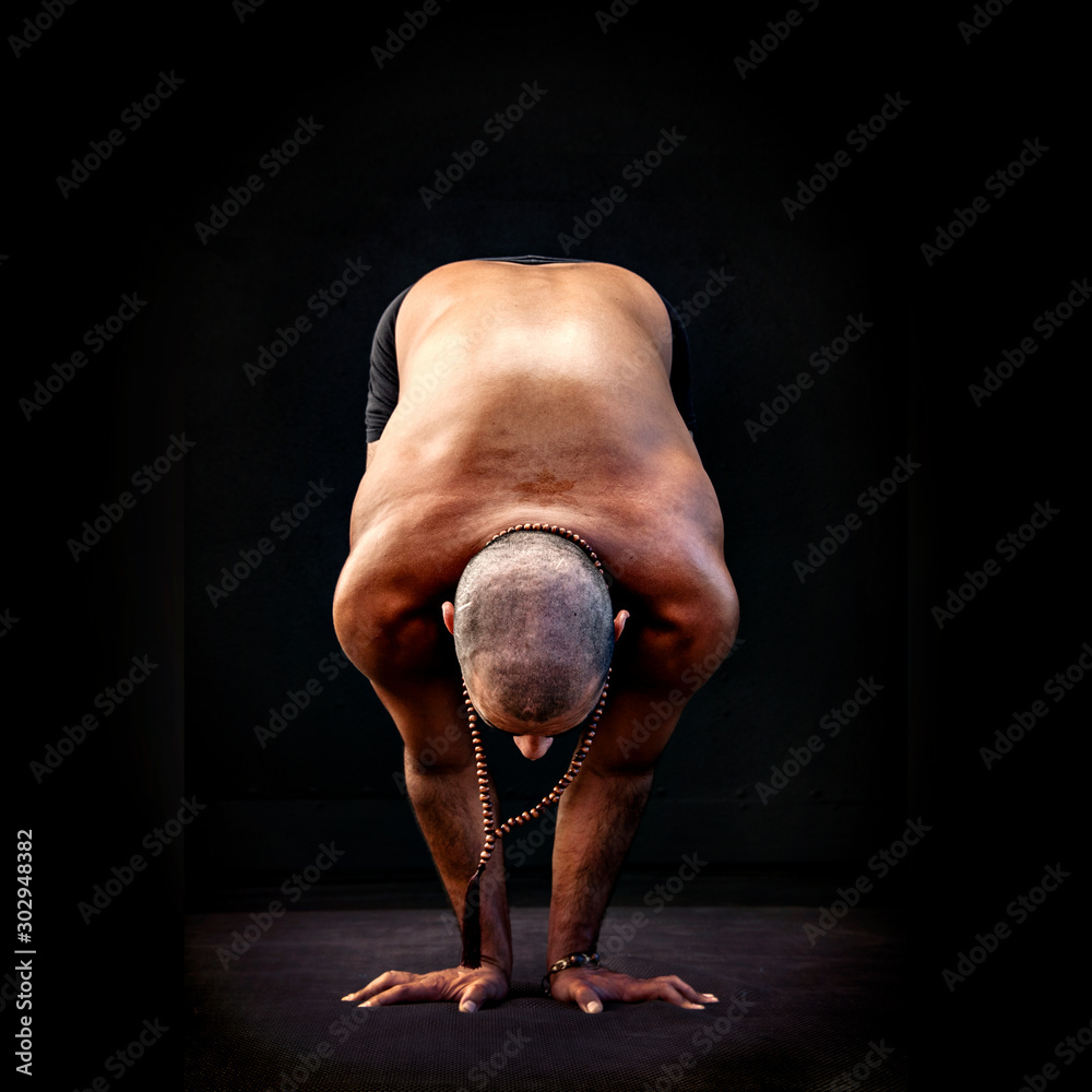 Fit hispanic man practicing yoga asana in a black studio. 