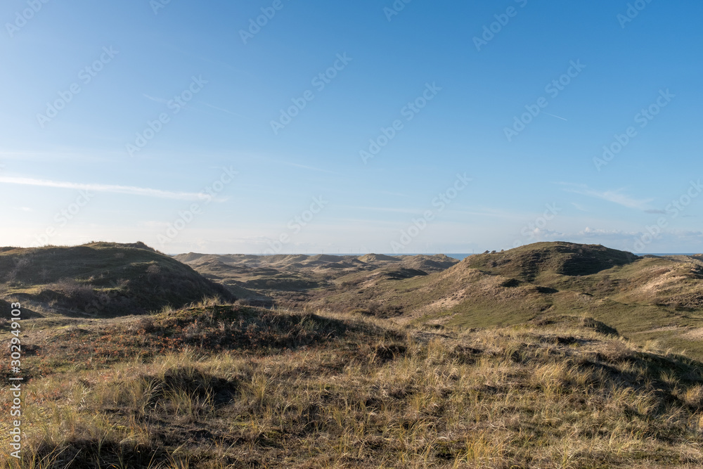 View from a high dune top on a valley with sea view between the dune tops and a blue sky