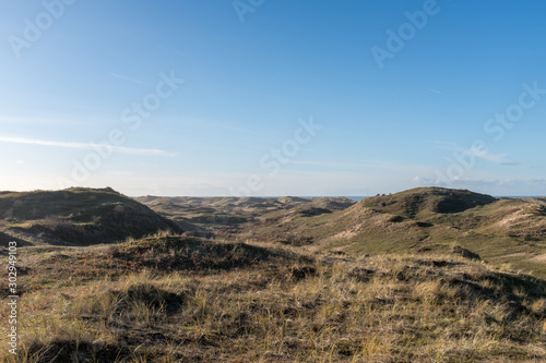 View from a high dune top on a valley with sea view between the dune tops and a blue sky