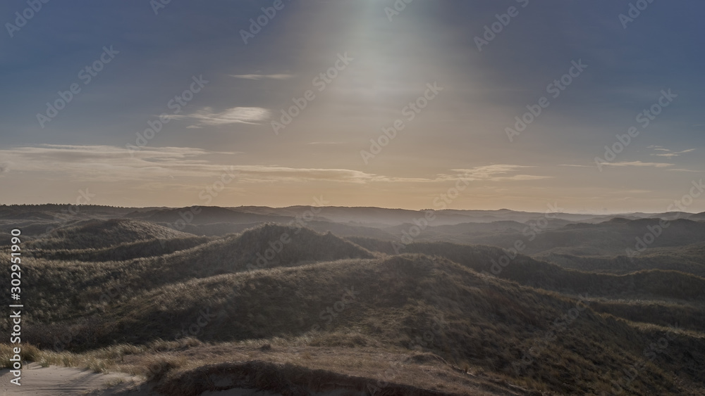 View over a dune landscape with backlight from a high point with the contours of an industrial area on the horizon View over a dune landscape with backlight from a high point with the contours of an industrial area on the horizon