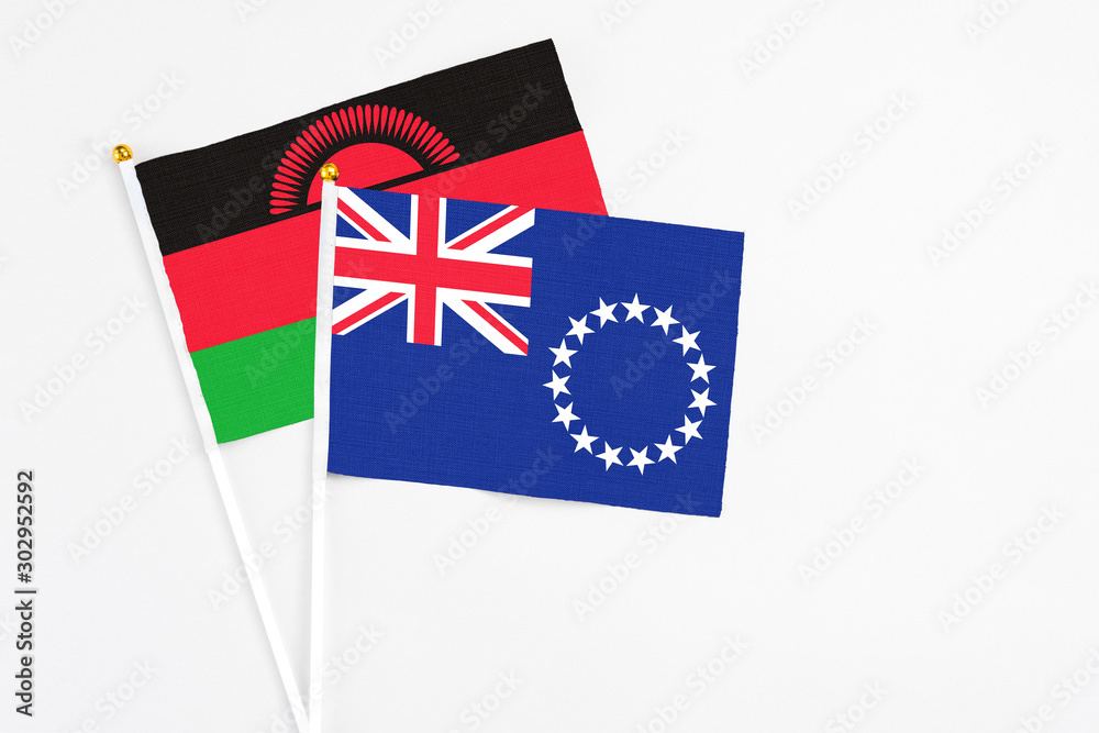 Fototapeta premium Cook Islands and Malawi stick flags on white background. High quality fabric, miniature national flag. Peaceful global concept.White floor for copy space.
