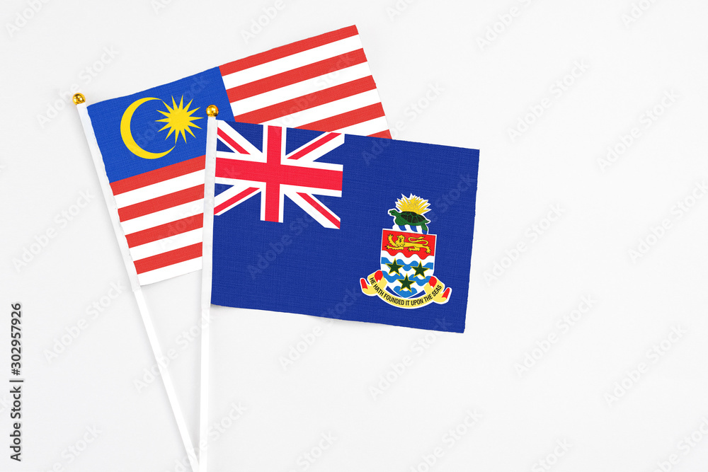 Fototapeta premium Cayman Islands and Malaysia stick flags on white background. High quality fabric, miniature national flag. Peaceful global concept.White floor for copy space.