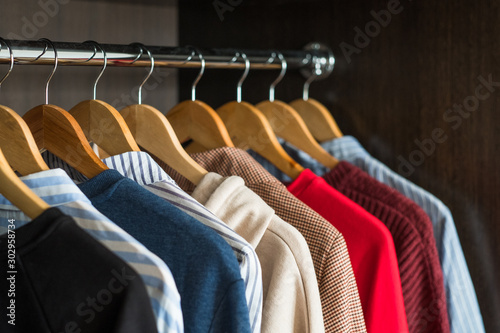 Hangers with different clothes in wardrobe closet. Shopping concept.
