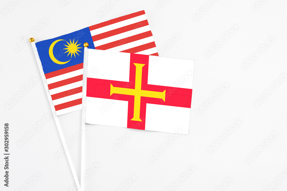 Guernsey and Malaysia stick flags on white background. High quality fabric, miniature national flag. Peaceful global concept.White floor for copy space.