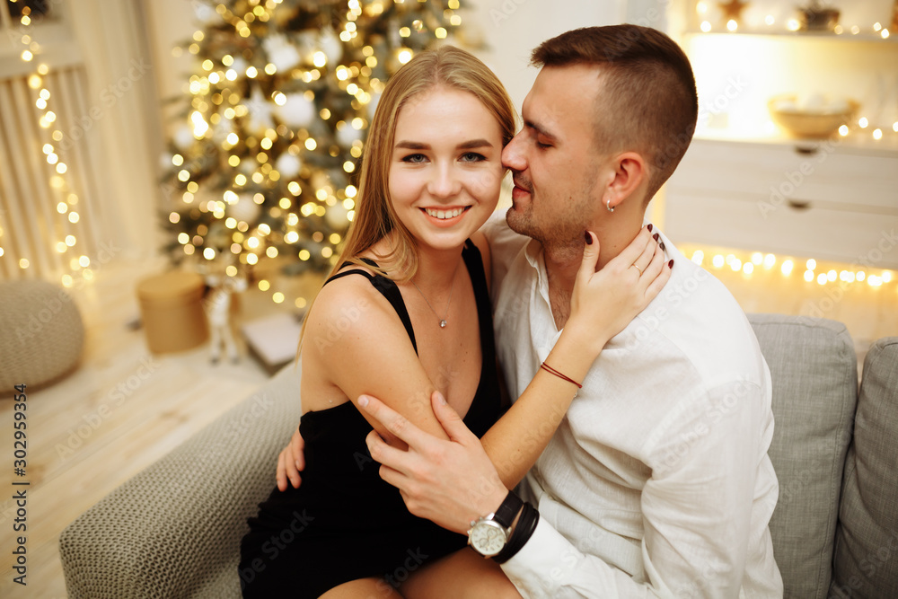 couple in love kisses and hugs on the sofa near the Christmas tree lights. New year's night. Christmas. couple in love kisses and hugs on the sofa near the Christmas tree lights. New year's night. Christmas.