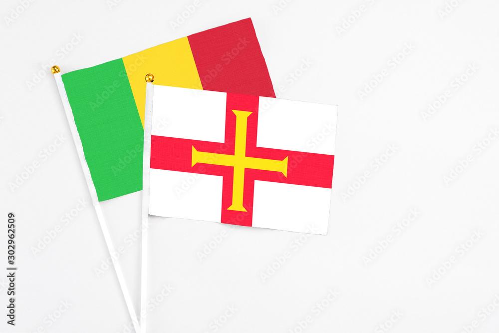 Guernsey and Mali stick flags on white background. High quality fabric, miniature national flag. Peaceful global concept.White floor for copy space.