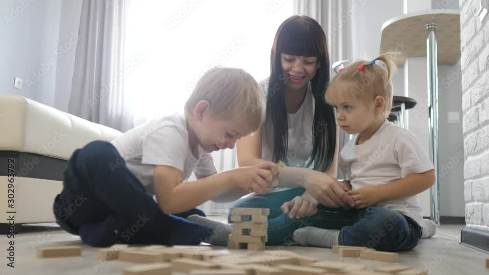 happy family a teamwork children collect a wooden pyramid concept. mom and kids play wooden constructor. mother and little boy and girl watch cartoons. kids play on the floor in a room indoors in happy family a teamwork children collect a wooden pyramid concept. mom and kids play wooden constructor. mother and little boy and girl watch cartoons. kids play on the floor in a room indoors in