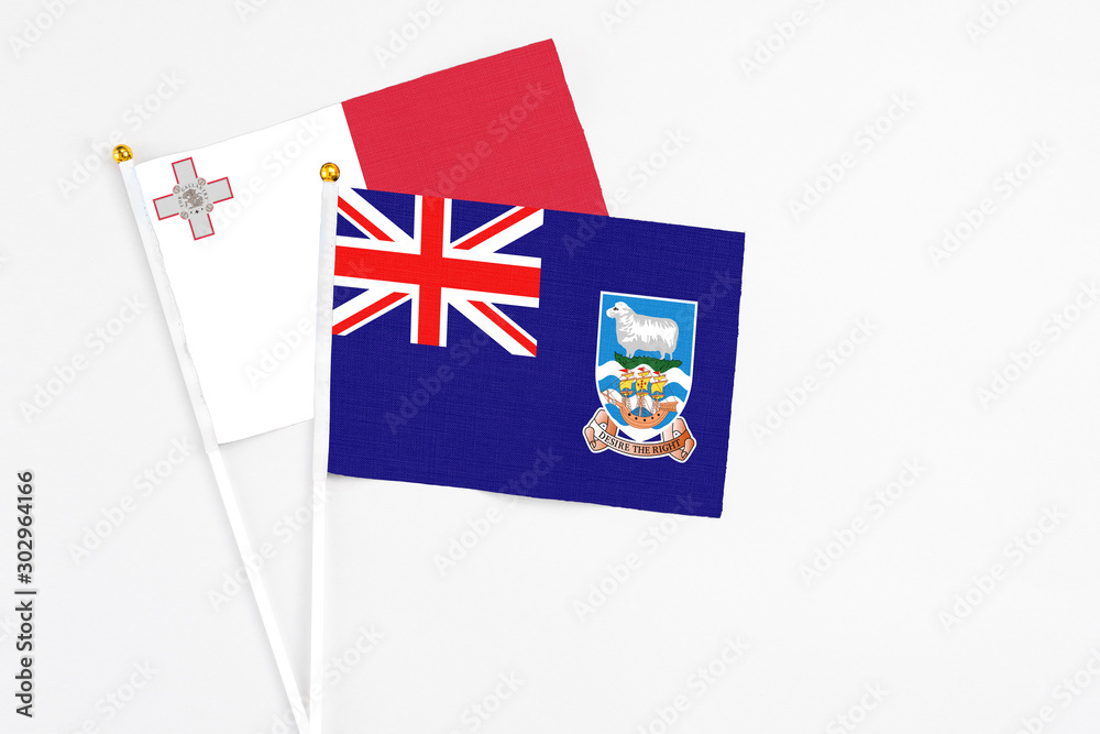 Fototapeta premium Falkland Islands and Malta stick flags on white background. High quality fabric, miniature national flag. Peaceful global concept.White floor for copy space.