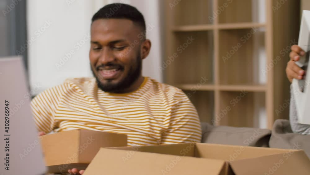 moving, people, repair and real estate concept - happy african american couple with photo frame and cardboard boxes sitting on sofa at new home moving, people, repair and real estate concept - happy african american couple with photo frame and cardboard boxes sitting on sofa at new home