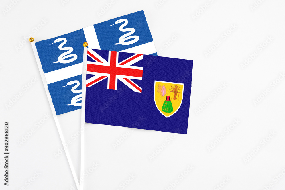Fototapeta premium Turks And Caicos Islands and Martinique stick flags on white background. High quality fabric, miniature national flag. Peaceful global concept.White floor for copy space.