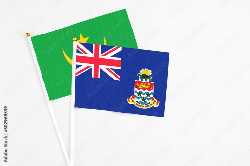 Fototapeta premium Cayman Islands and Mauritania stick flags on white background. High quality fabric, miniature national flag. Peaceful global concept.White floor for copy space.